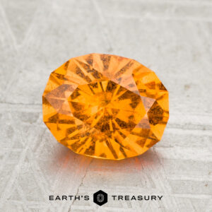 A 2.08-carat Spessartine Garnet gemstone rests on a textured gray surface with the text "EARTH'S TREASURY" at the bottom.