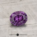 A 0.81-carat color-change garnet, round-cut and purple, is showcased on a textured gray surface with "Earth's Treasury" written below.
