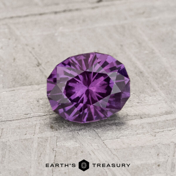 0.81-Carat Color-Change Garnet A 0.81-carat color-change garnet, round-cut and purple, is showcased on a textured gray surface with "Earth's Treasury" written below.