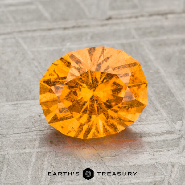 2.05-Carat Spessartine Garnet A faceted, oval-cut 2.05-carat Spessartine garnet is displayed on a gray textured surface with the text "EARTH'S TREASURY" below it.