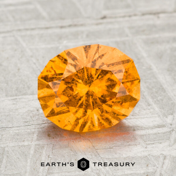 2.05-Carat Spessartine Garnet A faceted, oval-cut 2.05-carat Spessartine garnet is displayed on a gray textured surface with the text "EARTH'S TREASURY" below it.