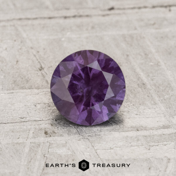 0.71-Carat Color-Change Garnet A 0.71-carat color-change garnet, round-cut and purple in hue, is shown on a light textured surface with "EARTH'S TREASURY" at the bottom.