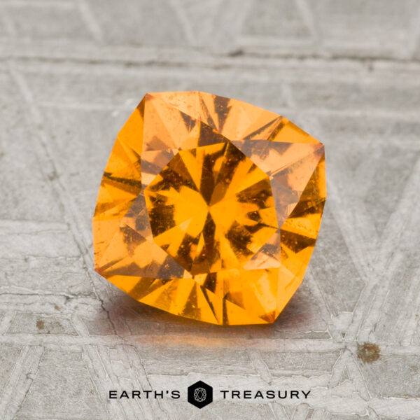 1.85-Carat Spessartine Garnet A 1.85-carat Spessartine garnet sits on a textured gray surface, with the "EARTH'S TREASURY" logo and text displayed beneath the gemstone.