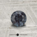 A 0.71-carat color-change garnet, round and faceted, rests on a textured, light surface with "EARTH'S TREASURY" displayed below.