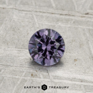 A 0.55-carat color-change garnet, expertly faceted and purple in hue, is displayed on a textured gray surface with the "Earth's Treasury" logo at the bottom.