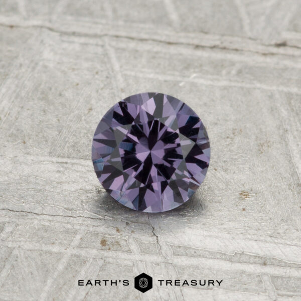 0.55-Carat Color-Change Garnet A 0.55-carat color-change garnet, expertly faceted and purple in hue, is displayed on a textured gray surface with the "Earth's Treasury" logo at the bottom.