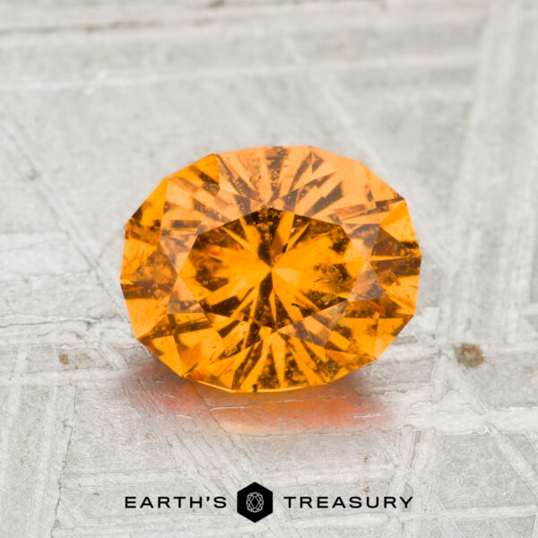 A 1.66-carat spessartine garnet, round brilliant-cut, is shown on a textured metallic surface with "EARTH'S TREASURY" beneath it.