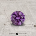 A 0.54-carat color-change garnet, round cut, is displayed on a textured, light surface with the "EARTH'S TREASURY" logo at the bottom.