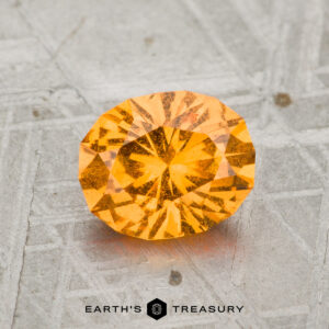 A 1.55-carat, faceted Spessartine Garnet gemstone is shown on a metallic patterned surface with the words "Earth's Treasury" below.