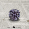 A 0.54-carat color-change garnet, round and faceted, is shown on a textured gray surface with the "EARTH'S TREASURY" logo at the bottom.