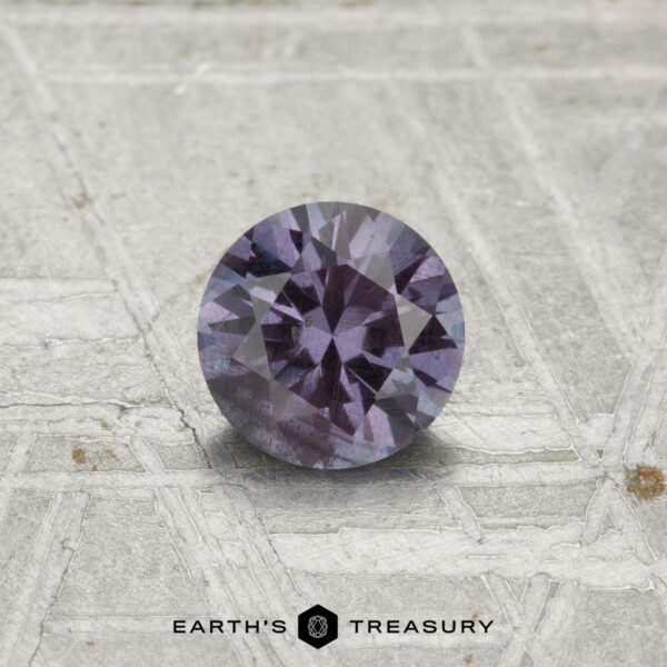 0.54-Carat Color-Change Garnet A 0.54-carat color-change garnet, round and faceted, is shown on a textured gray surface with the "EARTH'S TREASURY" logo at the bottom.