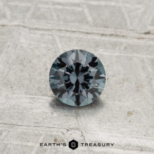 A 0.40-carat color-change garnet cut in a round, faceted shape is showcased on a light gray textured surface with the text "Earth's Treasury" at the bottom.