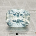 A faceted, pale blue 3.80-carat Montana Sapphire in a rectangular cut rests on a textured surface with "EARTH'S TREASURY" below.