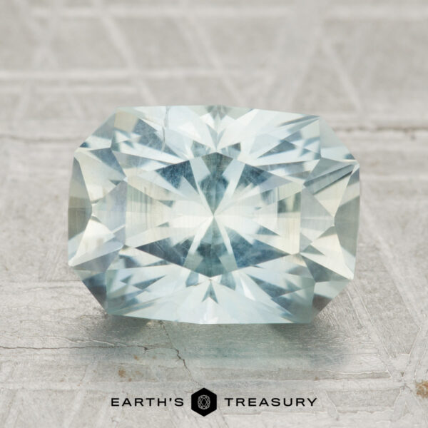 3.80-Carat Montana Sapphire A faceted, pale blue 3.80-carat Montana Sapphire in a rectangular cut rests on a textured surface with "EARTH'S TREASURY" below.