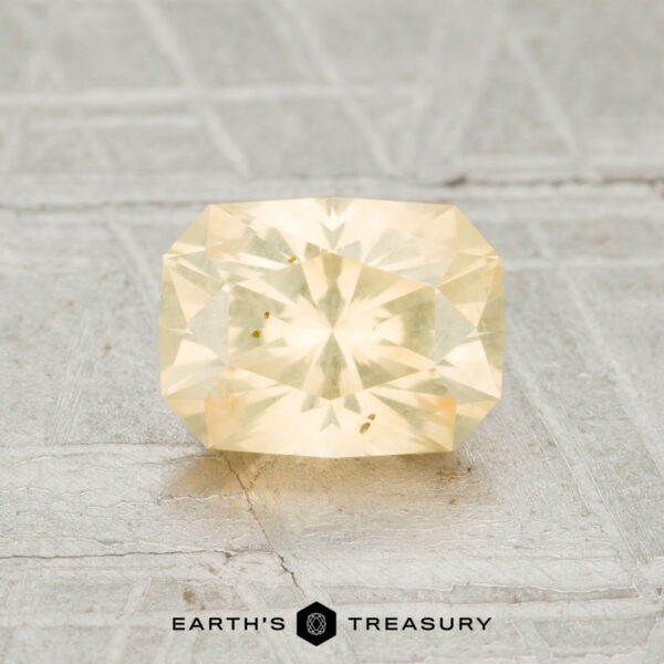 1.35-Carat Light Peach-Yellow Montana Sapphire A 1.35-carat rectangular, pale yellow Montana sapphire is shown on a textured gray surface with the Earth's Treasury logo at the bottom.