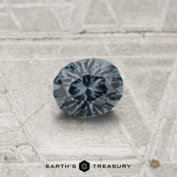 0.44-Carat Color-Change Garnet A 0.44-carat color-change garnet, round and faceted in dark gray, is shown on a textured light gray surface with "EARTH'S TREASURY" text at the bottom.