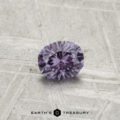 A round, faceted 0.43-carat color-change garnet sits on a textured gray surface, with "EARTH'S TREASURY" printed at the bottom.