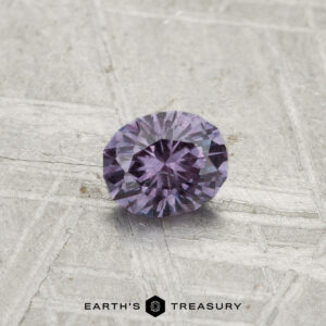 A round, faceted 0.43-carat color-change garnet sits on a textured gray surface, with "EARTH'S TREASURY" printed at the bottom.