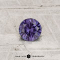 A 0.42-carat color-change garnet with a round cut is displayed on a textured light gray surface, featuring the text "Earth's Treasury" at the bottom.