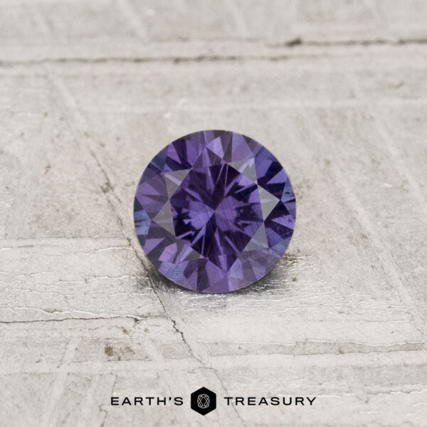 0.42-Carat Color-Change Garnet A 0.42-carat color-change garnet with a round cut is displayed on a textured light gray surface, featuring the text "Earth's Treasury" at the bottom.
