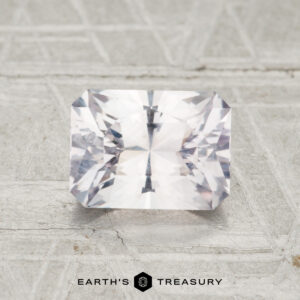 A 1.68-carat rectangular faceted Montana sapphire is displayed on a light textured surface with the "EARTH'S TREASURY" logo and text below it.