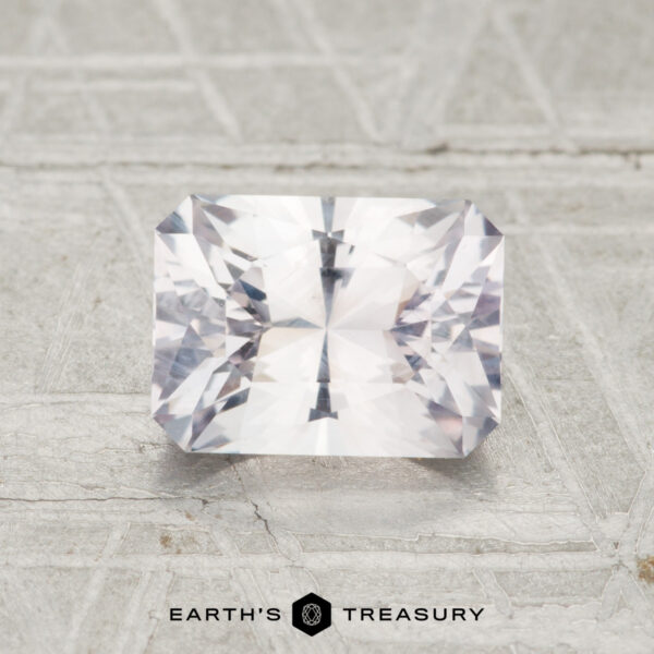 1.68-Carat Near-Colorless Montana Sapphire A 1.68-carat rectangular faceted Montana sapphire is displayed on a light textured surface with the "EARTH'S TREASURY" logo and text below it.
