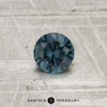 A 0.42-carat color-change garnet gemstone, round and faceted, is displayed on a textured light gray surface with "EARTH'S TREASURY" at the bottom.