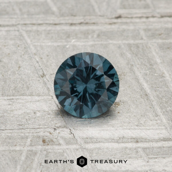 0.42-Carat Color-Change Garnet A 0.42-carat color-change garnet gemstone, round and faceted, is displayed on a textured light gray surface with "EARTH'S TREASURY" at the bottom.