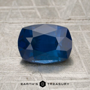 A 1.78-carat deep blue Vietnamese sapphire (unheated) with a cushion cut rests on a textured gray surface. "EARTH'S TREASURY" appears at the bottom.