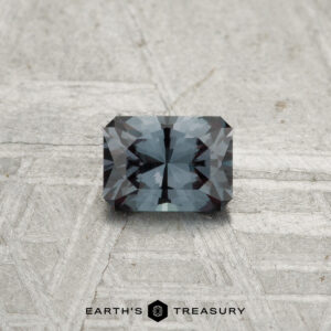A 0.39-carat color-change garnet, cut in a rectangular faceted shape, rests on a textured light surface with the "EARTH'S TREASURY" logo beneath it.