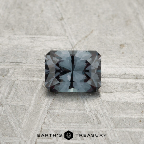 0.39-Carat Color-Change Garnet A 0.39-carat color-change garnet, cut in a rectangular faceted shape, rests on a textured light surface with the "EARTH'S TREASURY" logo beneath it.
