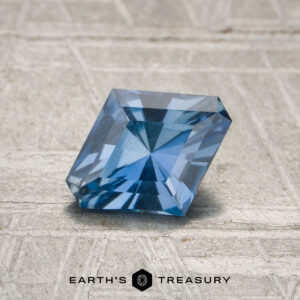 A 0.92-carat medium blue Malawi sapphire (unheated) with rectangular facets is displayed on a textured light surface, featuring the Earth's Treasury logo and text below.