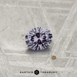 A 0.28-carat color-change garnet, round and faceted, is displayed on a textured gray surface with "Earth's Treasury" at the bottom.