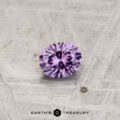 A 0.28-carat color-change garnet, round brilliant-cut, sits on a textured light gray surface with the "Earth's Treasury" logo below.