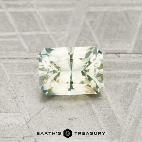 0.88-Carat Mint Green Montana Sapphire A 0.88-carat Montana sapphire with rectangular facets and light green-yellow hues rests on a textured gray surface, with the "Earth’s Treasury" logo and text below.