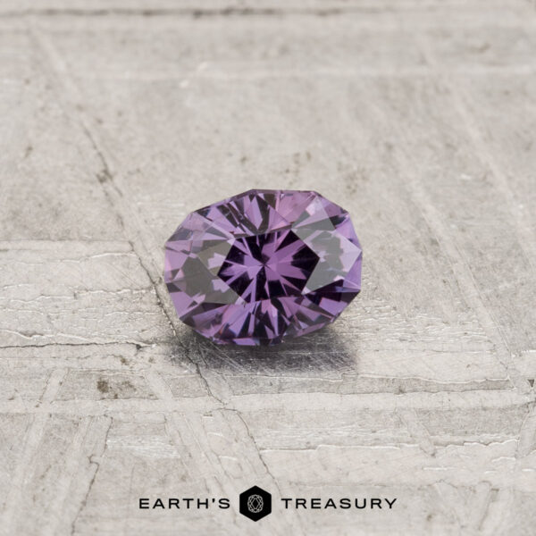 0.30-Carat Color-Change Garnet A 0.30-carat color-change garnet with a round, faceted cut rests on a textured gray surface featuring the "Earth's Treasury" logo at the bottom.