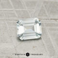 A 0.62-carat Montana sapphire with an emerald cut is displayed on a textured gray surface, with "EARTH'S TREASURY" text at the bottom.