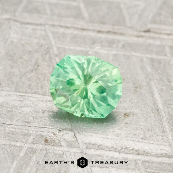 0.43-Carat Kornerupine A 0.43-carat, round brilliant-cut green Kornerupine gemstone rests on a light, textured surface with "EARTH'S TREASURY" at the bottom.
