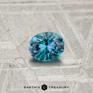 A 0.33-carat Kornerupine gemstone rests on a textured, geometric-patterned surface with "EARTH'S TREASURY" at the bottom.