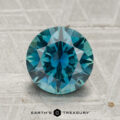 A 2.33-carat round brilliant-cut Montana sapphire is displayed on a textured gray surface, with the "Earth's Treasury" logo and text beneath it.