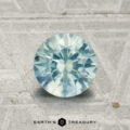 A 1.22-carat Montana Sapphire, round-cut and light blue, is shown on a textured gray surface with the Earth's Treasury logo at the bottom.