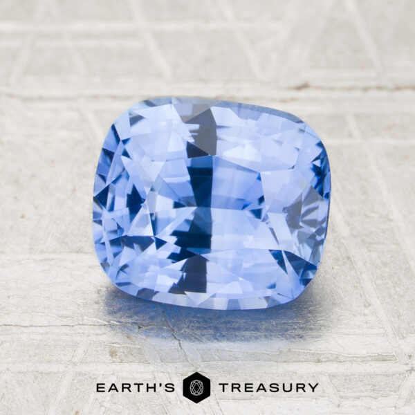 2.37-Carat Sapphire (Heated) A 2.37-carat sky blue Ceylon sapphire (heated), faceted in a cushion cut, is displayed on a textured light surface with the "Earth's Treasury" logo at the bottom of the image.