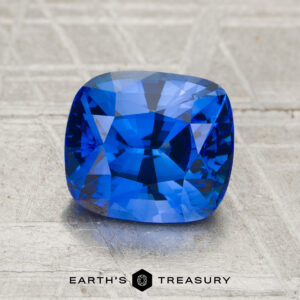 A 2.34-carat heated sapphire with a cushion cut is displayed on a textured surface, with "Earth’s Treasury" written below.