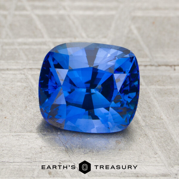 2.34-Carat Sapphire (Heated) A 2.34-carat heated sapphire with a cushion cut is displayed on a textured surface, with "Earth’s Treasury" written below.