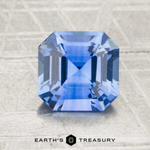 A 2.29-carat heated sapphire with a square step cut is shown on a textured surface, with "Earth's Treasury" written below it.