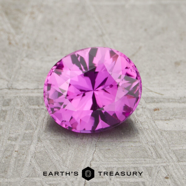 1.15-Carat Pink Ceylon Sapphire (Heated) A 1.15-carat Pink Ceylon Sapphire (Heated), cut in a faceted oval shape, is displayed on a textured gray surface with the Earth’s Treasury logo beneath it.