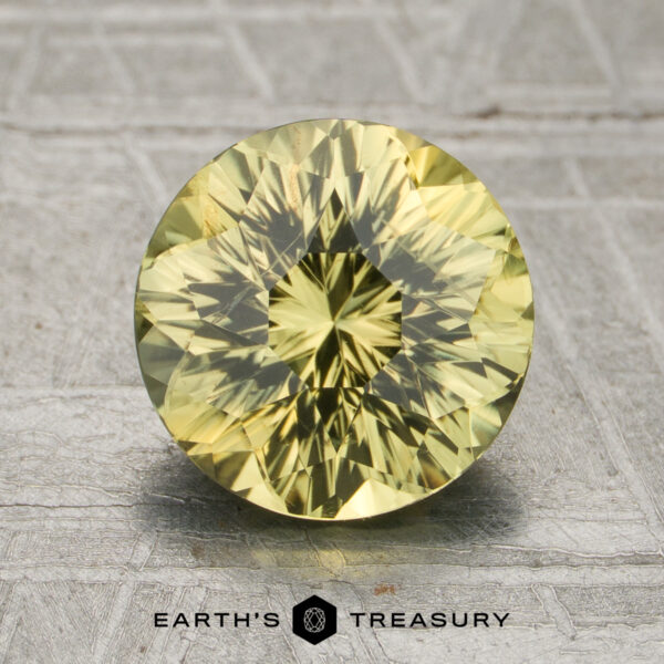 2.29-Carat Greenish-Yellow Kenya Sapphire (Unheated) A 2.29-carat unheated greenish-yellow Kenya sapphire, round and faceted, is displayed upright on a gray patterned surface with the "Earth's Treasury" text and logo below it.