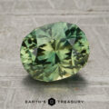 A 2.31-carat yellow-green particolored unheated Vietnam sapphire is displayed on a textured surface with the Earth’s Treasury logo beneath it.