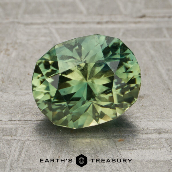 2.31-Carat Yellow-Green Particolored Vietnam Sapphire (Unheated) A 2.31-carat yellow-green particolored unheated Vietnam sapphire is displayed on a textured surface with the Earth’s Treasury logo beneath it.