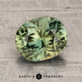 A faceted, oval-shaped green 2.31-carat unheated Vietnam sapphire displayed on a textured gray surface with the text "EARTH'S TREASURY" below it.